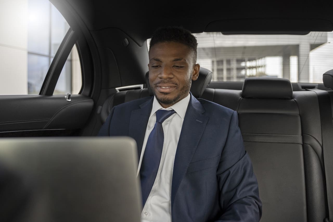 Homme d'affaires africain élégant travaillant sur son ordinateur portable dans le siège arrière d'un taxi.